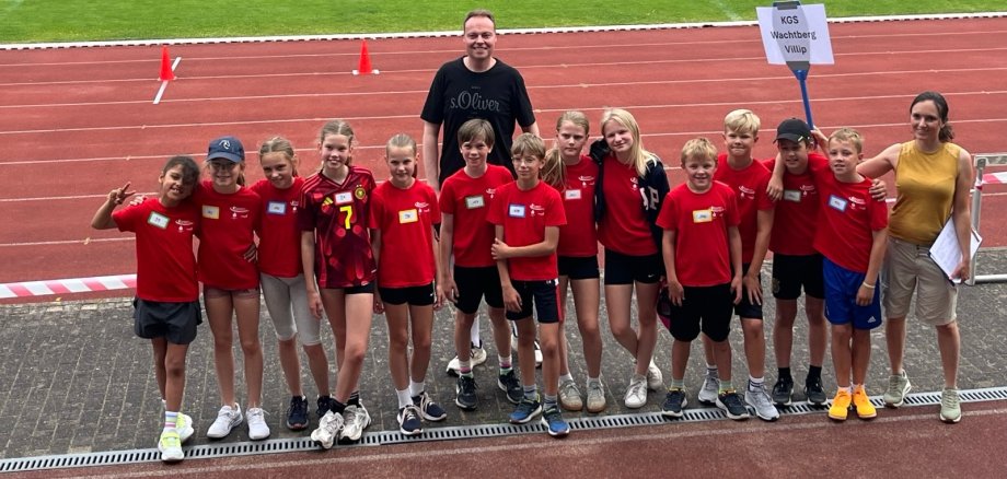 Eine Gruppe Kinder in Sportkleidung und zwei Erwachsene im Stadion